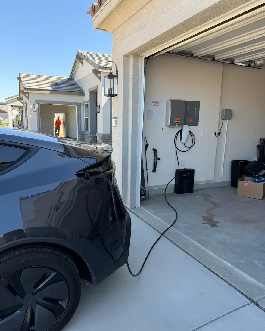Tesla Wall Connector hardwired inside an attached garage, with an EV plugged in and charging.