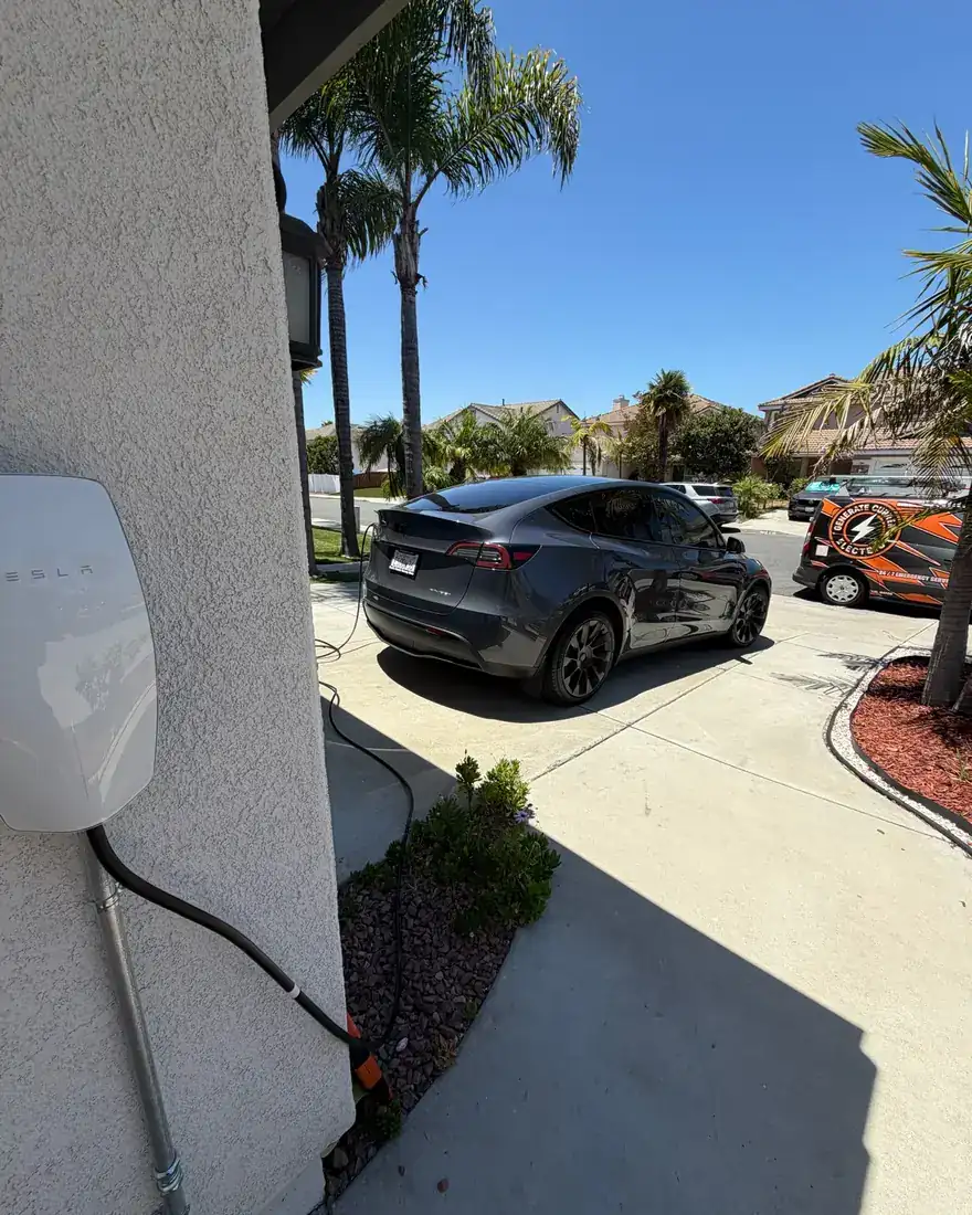 Exterior-mounted EV charger beside a driveway with an electric vehicle parked in front of the house.