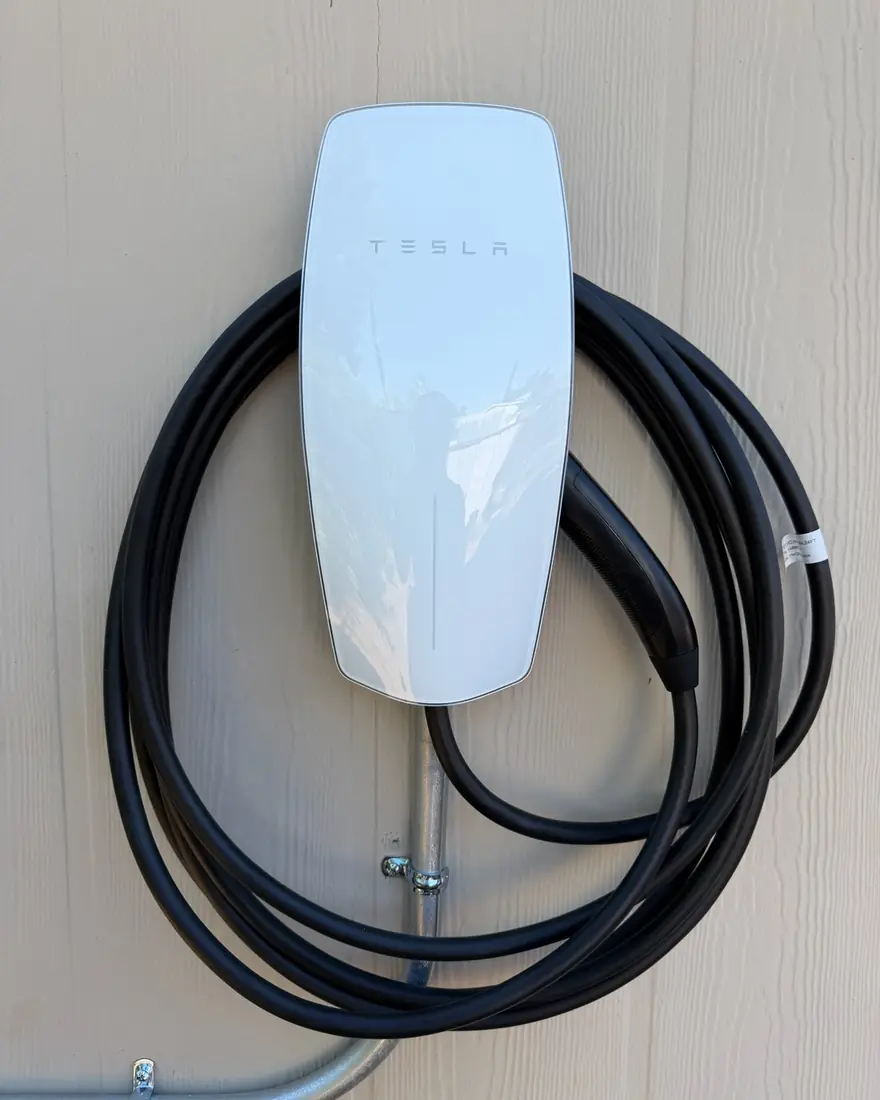 Tesla Wall Connector mounted on a garage wall with rigid conduit run to the unit.