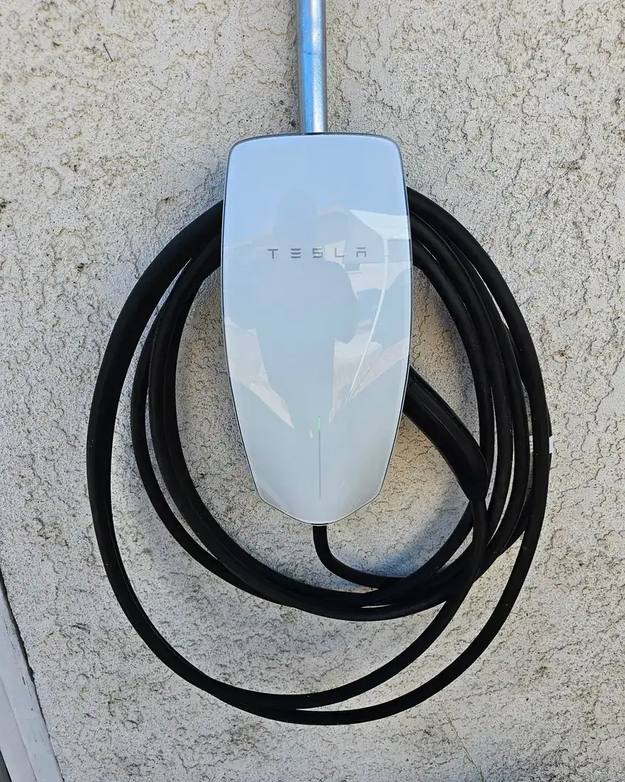 Tesla Wall Connector mounted on a stucco exterior wall with conduit dropping down from above.